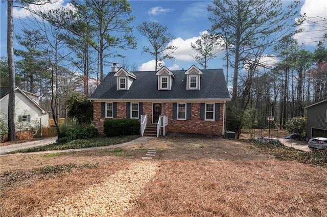 cape cod home with a shingled roof, cooling unit, and brick siding