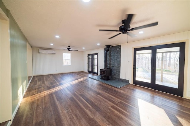 unfurnished living room featuring wood finished floors, a wood stove, ceiling fan, an AC wall unit, and french doors