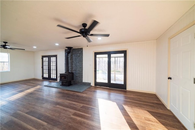 unfurnished living room featuring baseboards, ceiling fan, french doors, a wood stove, and wood finished floors