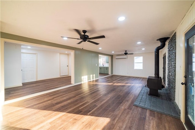 unfurnished living room with a wall unit AC, wood finished floors, a wood stove, recessed lighting, and ceiling fan