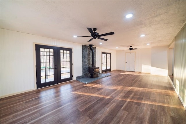 unfurnished living room featuring wood finished floors, a wood stove, french doors, and a textured ceiling