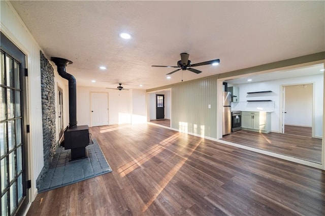 unfurnished living room featuring a ceiling fan, wood finished floors, a wood stove, recessed lighting, and a textured ceiling