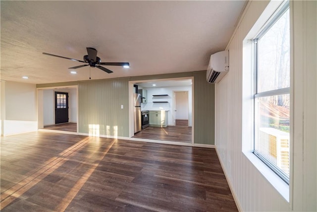 unfurnished living room featuring a ceiling fan, an AC wall unit, wood finished floors, and baseboards