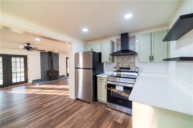 kitchen featuring dark wood-type flooring, wall chimney range hood, stainless steel appliances, light countertops, and a wood stove