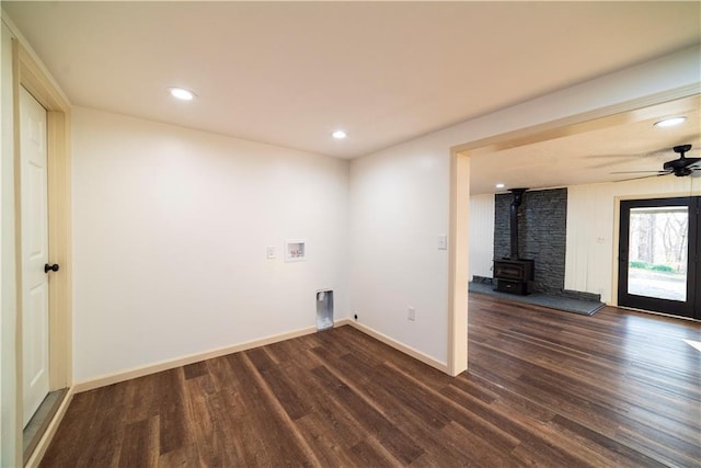 clothes washing area featuring baseboards, laundry area, hookup for a washing machine, a wood stove, and dark wood-style flooring