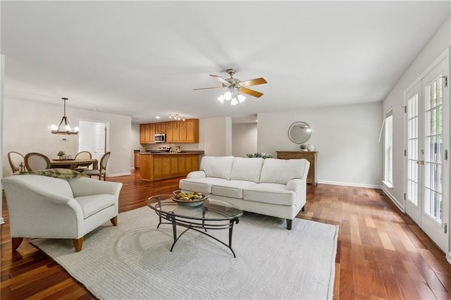 living area with dark wood-style flooring, a wealth of natural light, and ceiling fan with notable chandelier