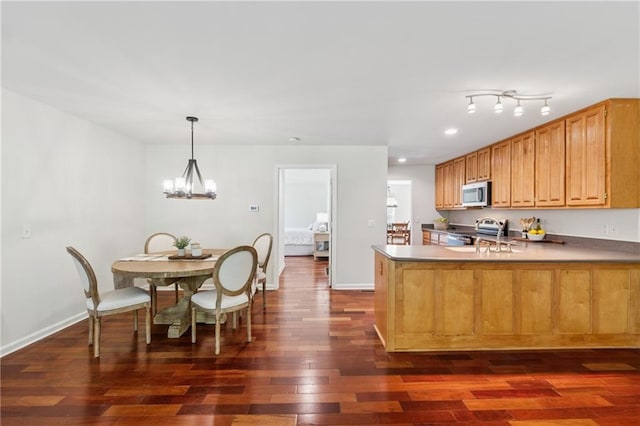 kitchen featuring appliances with stainless steel finishes, an inviting chandelier, dark wood finished floors, a peninsula, and baseboards