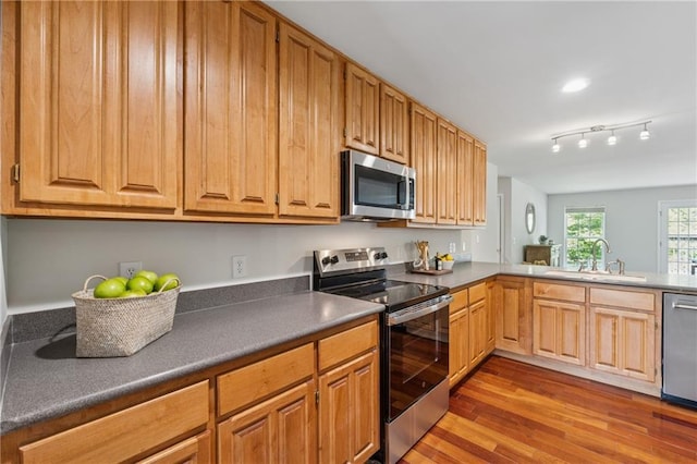 kitchen featuring a sink, appliances with stainless steel finishes, wood finished floors, and dark countertops