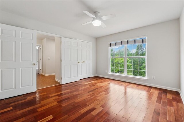 unfurnished bedroom featuring baseboards, a ceiling fan, wood finished floors, and a closet