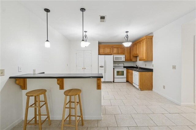 kitchen with dark countertops, a sink, white appliances, a breakfast bar area, and a peninsula
