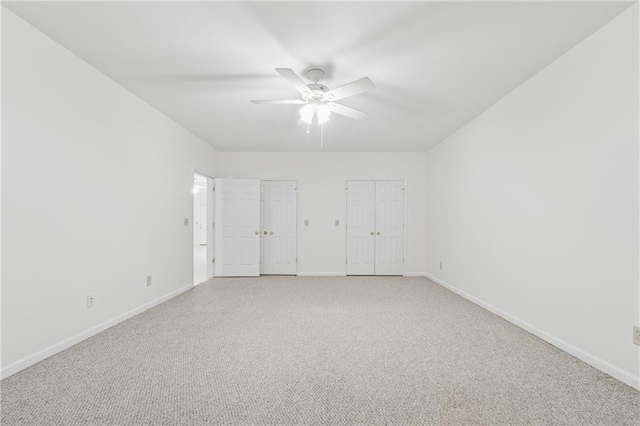 unfurnished bedroom with baseboards, ceiling fan, two closets, and light carpet