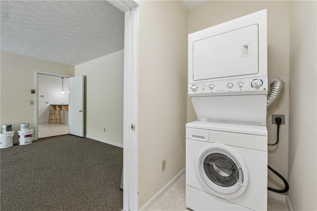 laundry area with laundry area, a textured ceiling, stacked washing maching and dryer, and baseboards