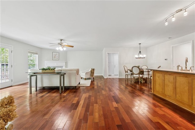 living area featuring dark wood-type flooring, baseboards, and ceiling fan with notable chandelier
