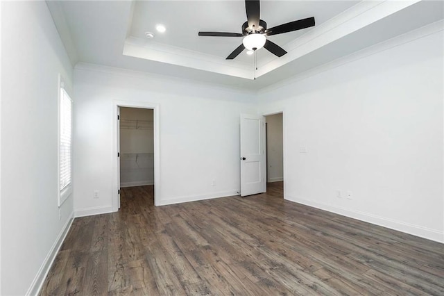 unfurnished bedroom with a walk in closet, baseboards, ornamental molding, wood finished floors, and a raised ceiling