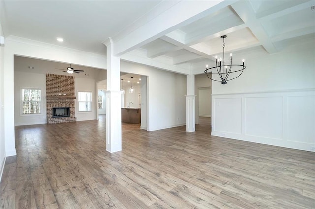 unfurnished living room with wood finished floors, beam ceiling, a brick fireplace, a decorative wall, and ceiling fan with notable chandelier