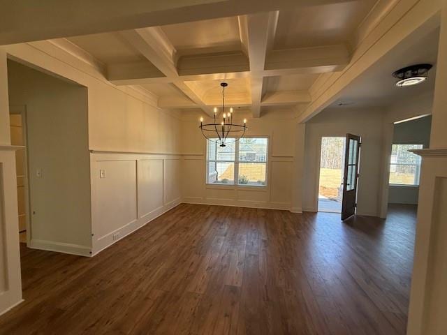 unfurnished dining area featuring dark wood finished floors, a notable chandelier, a decorative wall, coffered ceiling, and beamed ceiling