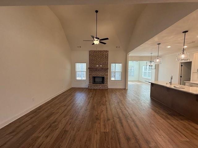 unfurnished living room featuring a brick fireplace, dark wood finished floors, a ceiling fan, and baseboards