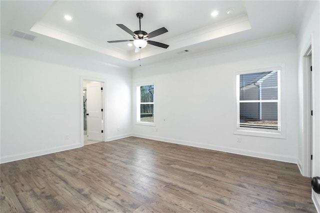 unfurnished room with a tray ceiling, wood finished floors, visible vents, and baseboards