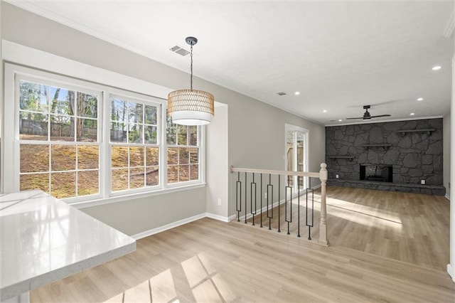 unfurnished dining area featuring visible vents, wood finished floors, a stone fireplace, baseboards, and ceiling fan