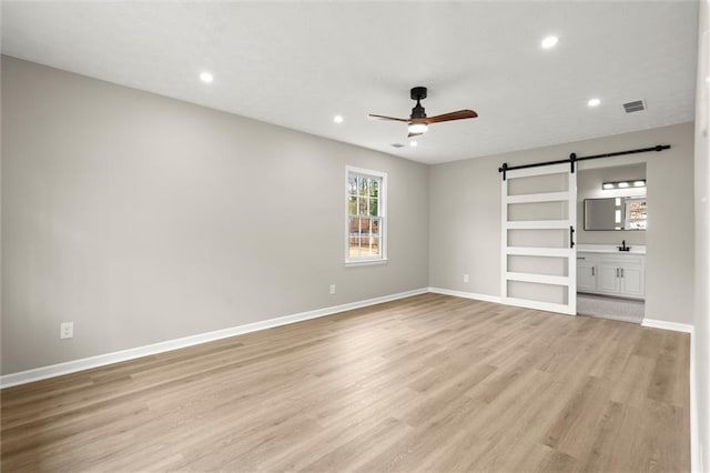 unfurnished room featuring recessed lighting, a barn door, light wood-style floors, baseboards, and ceiling fan