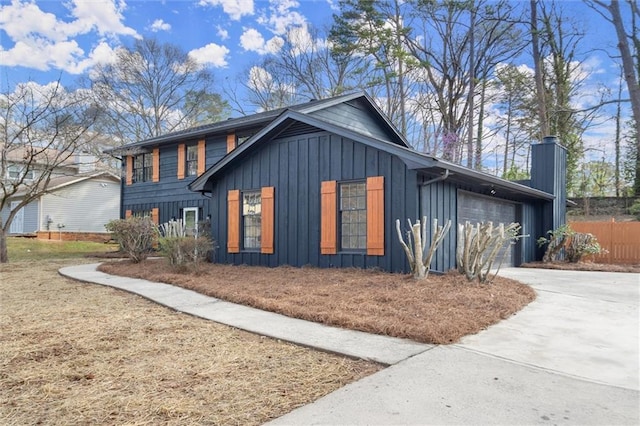 view of side of home with fence, a chimney, concrete driveway, a garage, and board and batten siding