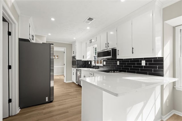 kitchen featuring tasteful backsplash, visible vents, a peninsula, stainless steel appliances, and white cabinetry