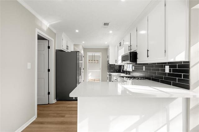 kitchen with visible vents, a peninsula, decorative backsplash, appliances with stainless steel finishes, and crown molding