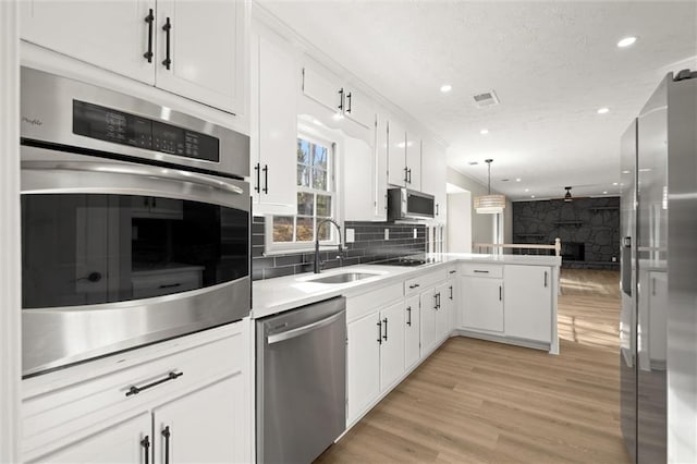 kitchen with open floor plan, a peninsula, stainless steel appliances, white cabinetry, and a sink