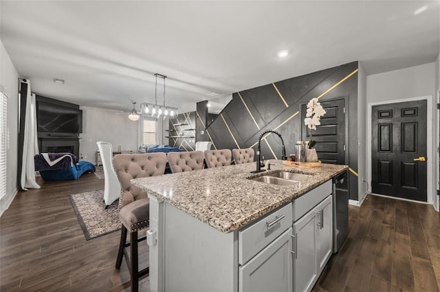 kitchen with sink, a breakfast bar area, dishwasher, hanging light fixtures, and a center island with sink