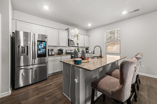 kitchen featuring sink, white cabinetry, appliances with stainless steel finishes, light stone countertops, and a kitchen island with sink