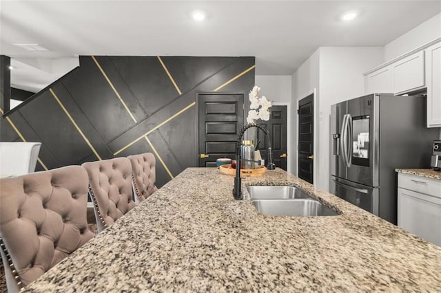 kitchen with white cabinetry, sink, light stone counters, and stainless steel refrigerator