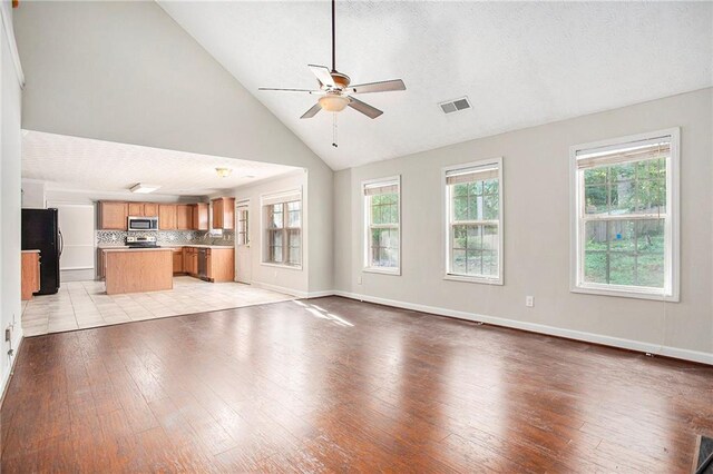 unfurnished living room with high vaulted ceiling, ceiling fan, and light hardwood / wood-style floors