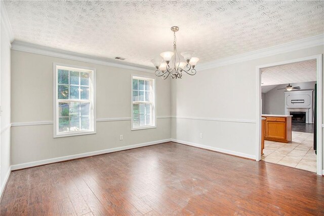 empty room with a textured ceiling, light hardwood / wood-style flooring, ornamental molding, and ceiling fan with notable chandelier