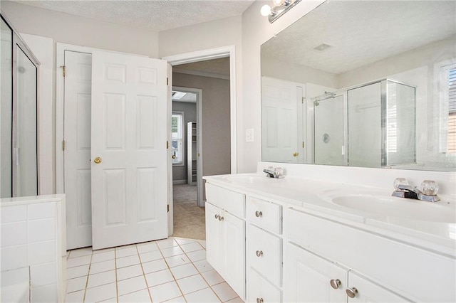 bathroom with a textured ceiling, vanity, tile patterned flooring, and walk in shower