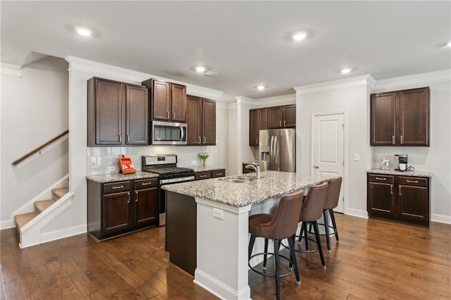 kitchen with sink, stainless steel appliances, a kitchen breakfast bar, light stone counters, and a center island with sink