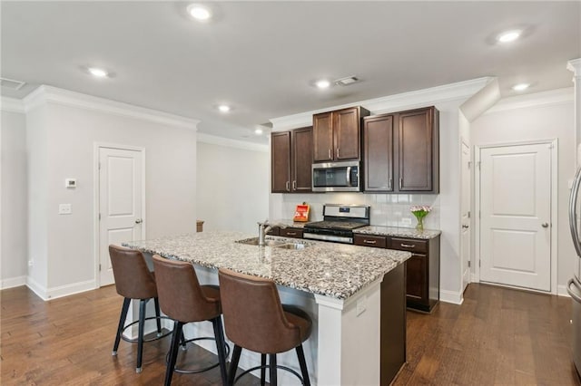 kitchen featuring appliances with stainless steel finishes, an island with sink, a breakfast bar area, backsplash, and dark hardwood / wood-style flooring