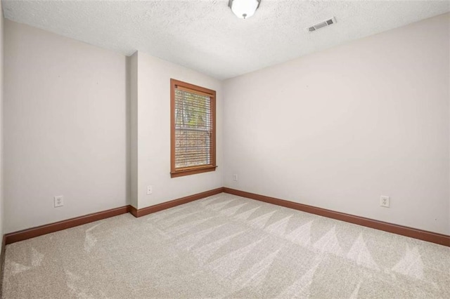 unfurnished room with a textured ceiling, carpet floors, visible vents, and baseboards