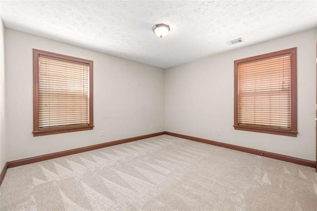 empty room with light carpet, a textured ceiling, visible vents, and baseboards