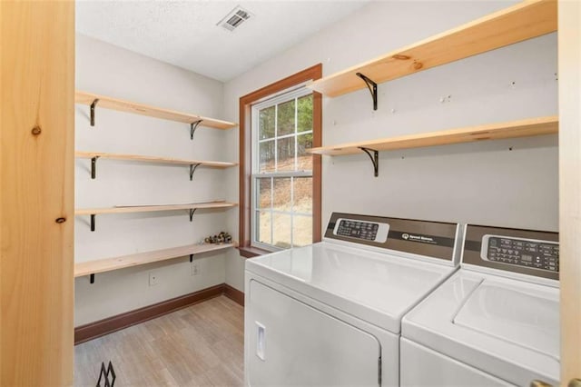 washroom with washing machine and clothes dryer, visible vents, light wood-style floors, laundry area, and baseboards