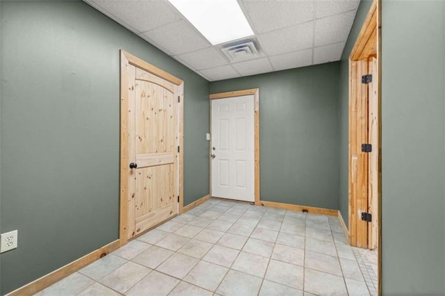 empty room with a paneled ceiling, visible vents, baseboards, and light tile patterned floors