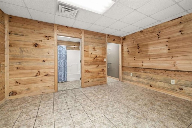 unfurnished room with wood walls, visible vents, and a drop ceiling