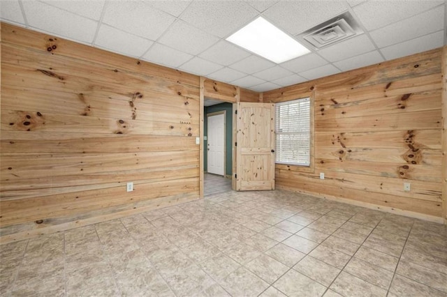 unfurnished room featuring a paneled ceiling, wooden walls, visible vents, and tile patterned floors