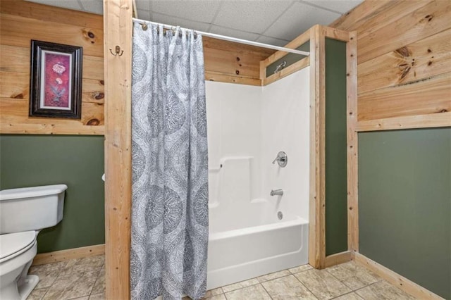 full bathroom featuring a drop ceiling, toilet, tile patterned floors, baseboards, and shower / tub combo with curtain