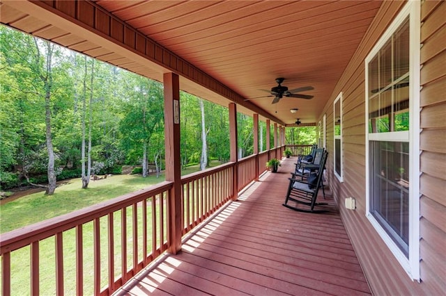 wooden deck featuring a ceiling fan, covered porch, and a lawn