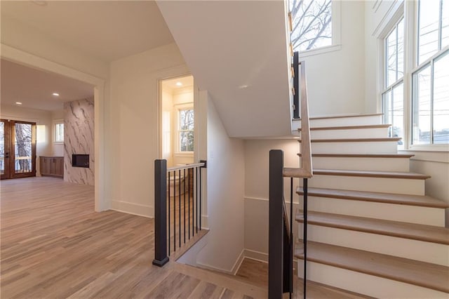 staircase with french doors, a fireplace, wood finished floors, and baseboards