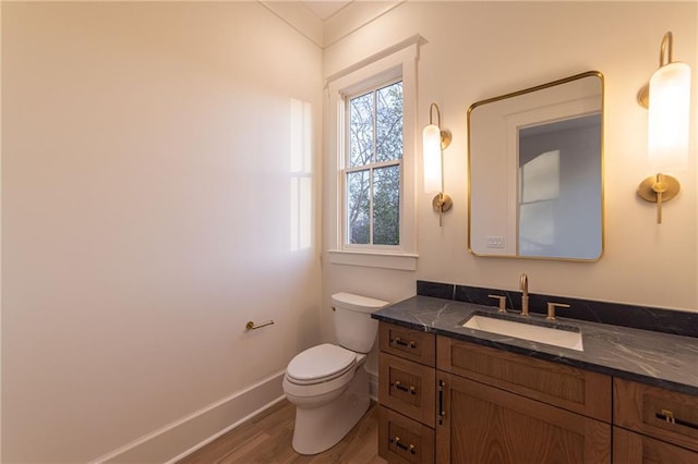 half bathroom with toilet, baseboards, wood finished floors, and vanity