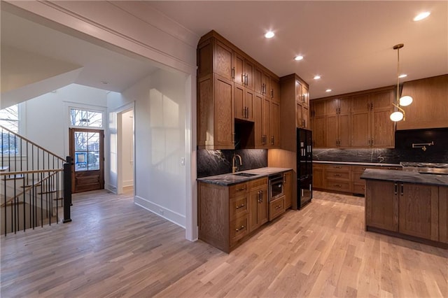 kitchen featuring a sink, backsplash, light wood finished floors, brown cabinetry, and dark countertops