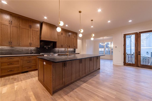 kitchen featuring a large island, brown cabinetry, a sink, and custom range hood