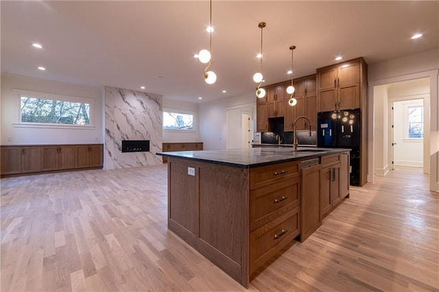 kitchen featuring a sink, a high end fireplace, dishwasher, brown cabinetry, and a center island with sink