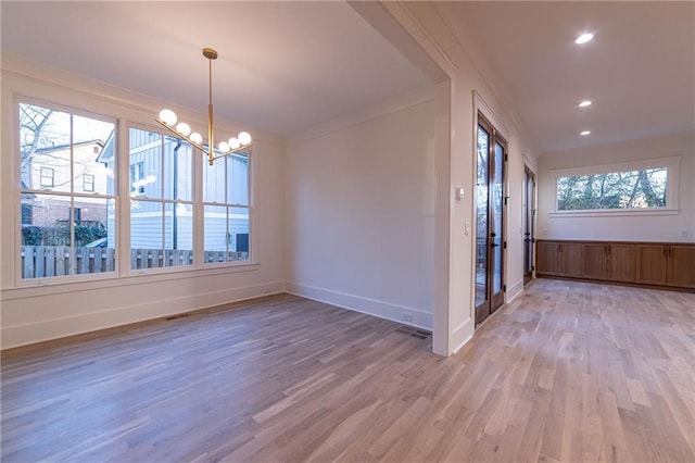 spare room featuring a healthy amount of sunlight, light wood-style floors, baseboards, and a notable chandelier